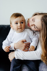 Son and mom sitting on couch at home and embracing celebrating mothers day looking at camera.