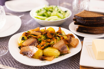 baked potatoes with chanterelles and bacon served with herbs and lightly salted cucumbers on table