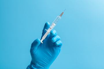 Medical glove. A hand in a blue medical glove holds a syringe. Isolated on a blue background.