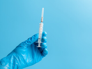Medical glove. A hand in a blue medical glove holds a syringe. Isolated on a blue background.