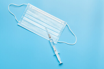Medical mask and syringe. A blue medical mask with a white elastic band and a syringe isolated on a blue background.