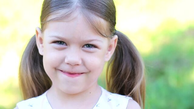Portrait of smiling and modest caucasian little girl of 6 years looking at camera outdoor summer