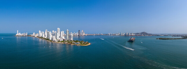 The modern skyscrapers in the Cartagena in Colombia with sea port and cargo ship aerial panorama view - obrazy, fototapety, plakaty