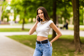 Portrait of young attractive woman speaking on mobile phone at summer green park.