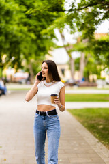 Caucasian business woman speaking by phone holding coffee to go. A successful European woman, talking on the phone, standing on modern office building background