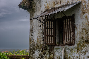 Interiors of a fort in Goa which shows the building architecture of Portuguese colonial influence having laterite stones, windows, doors and tiled roofs with the Monsoon sky in background