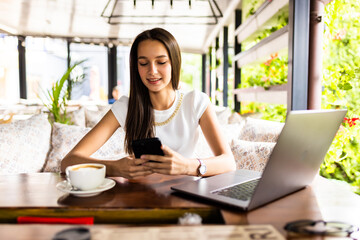 Fototapeta premium Portrait image of a young woman holding and using mobile phone and laptop in cafe