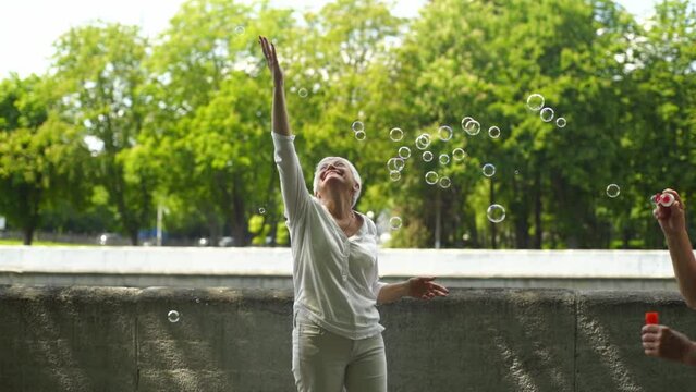 Many soap bubbles surround a happy elderly woman in white on a sunny summer day