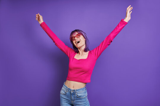 Happy young woman stretching out hands while standing against purple background
