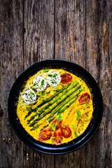 Tasty breakfast. Omelette  with green asparagus, goat cheese, pepper and cherry tomatoes served on black plate on wooden table
