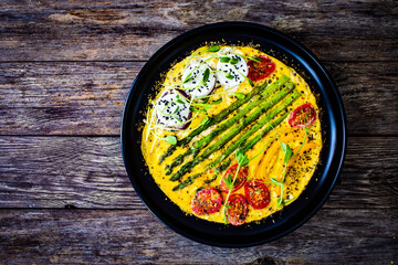 Tasty breakfast. Omelette  with green asparagus, goat cheese, pepper and cherry tomatoes served on...