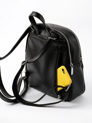 view from the back on a black leather women's backpack on a white background. the back pocket is open, a yellow mobile phone sticks out from there