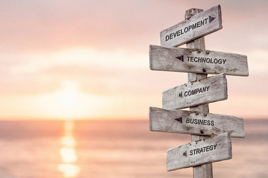 development technology company business strategy text engraved on wooden signpost by the ocean during sunset.