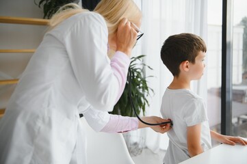 Doctor pediatrician examines child. Female doctor puts a stethoscope to a child's chest and listens to the little boy's heartbeat and lungs. Concept of health care and pediatric medical examination.