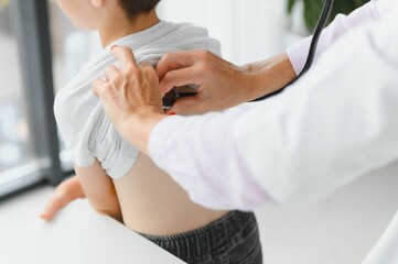 Pediatrician listening to breathing in the lungs and heartbeat with stethoscope. Portrait of adorable little boy visiting doctor.