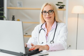 Shot of a female doctor working while sitting at desk in front of laptop