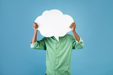 Unrecognizable african american young guy holding an empty speech bubble in front of his head, blue...
