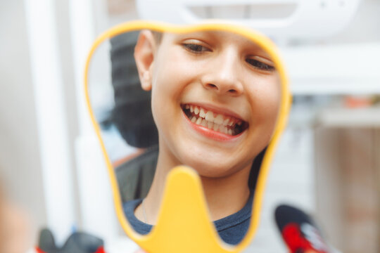 boy looks in the mirror with a toothy smile, sitting on a chair with a dentist in the dental office.