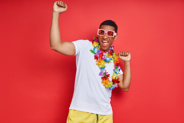 Handsome young man in Hawaiian necklace dancing against red background