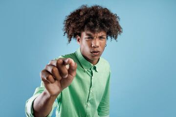 Young african amerian guy watching something on virtual screen and bringing closer, standing over blue studio background