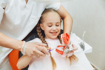 a male dentist in a medical uniform shows a little girl how to properly brush her teeth on a jaw...