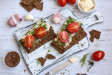 Top view of rye toasts with cheese, tomatoes and dill on a light board