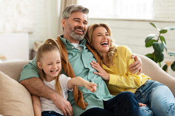 Middle Aged Parents Hugging Little Daughter Laughing Bonding At Home