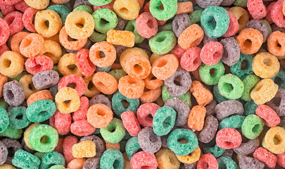Fototapeta na wymiar Delicious and nutritious fruit cereal loops as background, top view. Healthy breakfast.