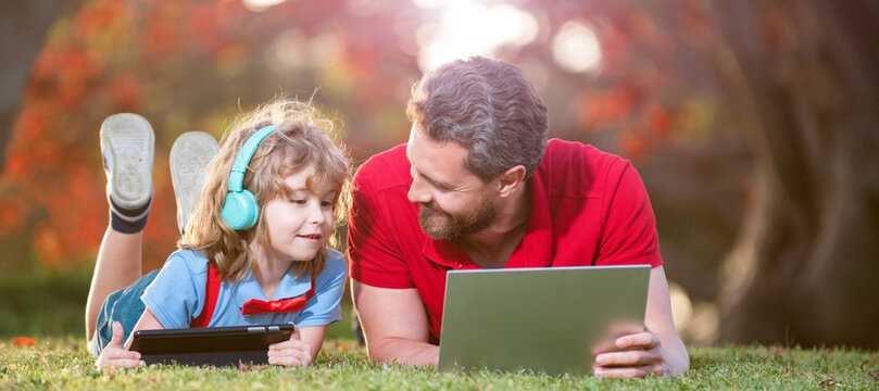 Banner of father on son school boy with laptop study online lying on grass, dad and son use laptop for video call or lesson listen music in headphones in park, education online