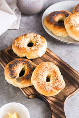 Bagels with poppy seeds and sesame on the board and butter in a bowl on the table. Vertical view