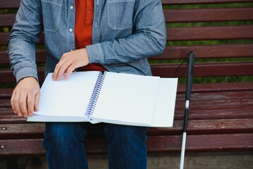 Blind man reading book on bench in park