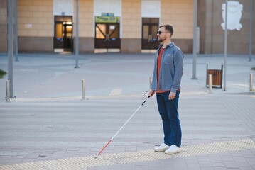 young blind man with white cane walking across the street in city