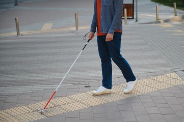 young blind man with white cane walking across the street in city