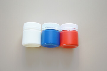 White, blue, red gouache paint in closed jars on a light background. Materials for creativity. Free space for text.