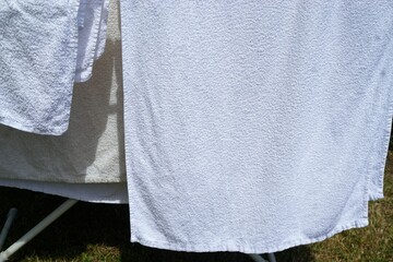 Weiße Frotteehandtücher zum Trocknen auf Wäscheständer im Garten bei Sonne im Frühling