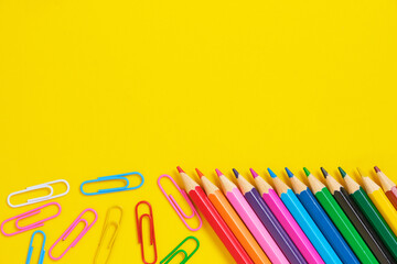 Colored pencils and paper clips yellow background.