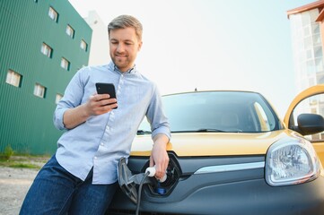 Handsome man using phone while car being charged