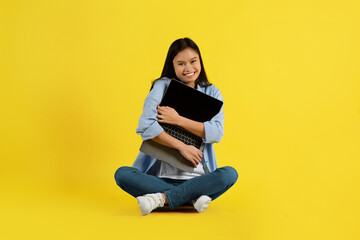 Cheerful glad young asian woman student with down syndrome sitting on floor, hugging laptop