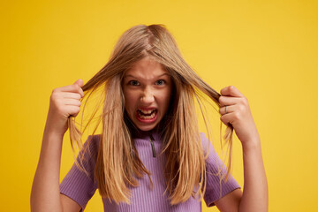Portrait of a young girl with an angry expression, on a clean yellow background, space for text