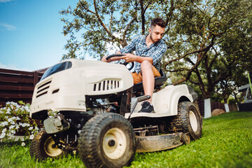 Fototapeta na wymiar Man using lawn tractor for mowing grass in garden. Landscaping works with professional tools