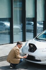 Handsome man using phone while car being charged