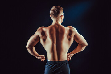 Fototapeta premium Rear view of healthy muscular young man with arms bent out isolated on black background