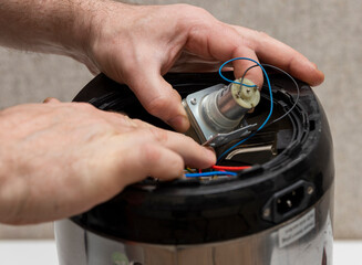 a man is engaged in repairing a faulty electric thermo pot, changing a faulty pump for water supply.
