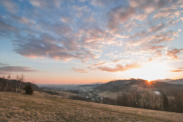 Fototapeta na wymiar Sunrise at the hills of the mountains and the village of Kozlovice in the foothills of the Beskydy Mountains in the Moravian-Silesian region of the Czech Republic. Colorful clouds with orange ball