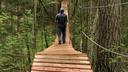 Rear view of male tourist crossing wooden suspension bridge in green forest. Stock footage. Back...