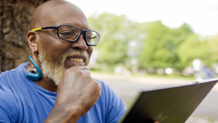 Smiling black male using a digital tablet device outdoors in a park