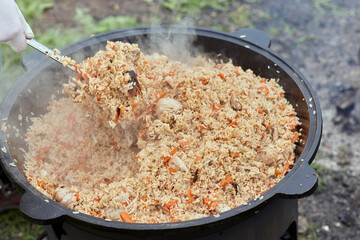 Cooking food or pilaf in a cauldron on fire. Cooking in cauldron on open fire in nature. Bowler on...
