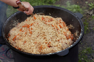 Cooking food or pilaf in a cauldron on fire. Cooking in cauldron on open fire in nature. Bowler on...
