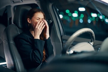 a frustrated, emotional, crying woman is sitting behind the wheel of a car with her seat belt fastened, crying, covering her face with her hands. Photography at night