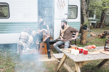 Young beautiful loving couple travelling across country in the van. Millennial man and woman in a travel camper. Cozy atmosphere, vacations vibe. Playing guitar, drinking tea, cooking on a campfire